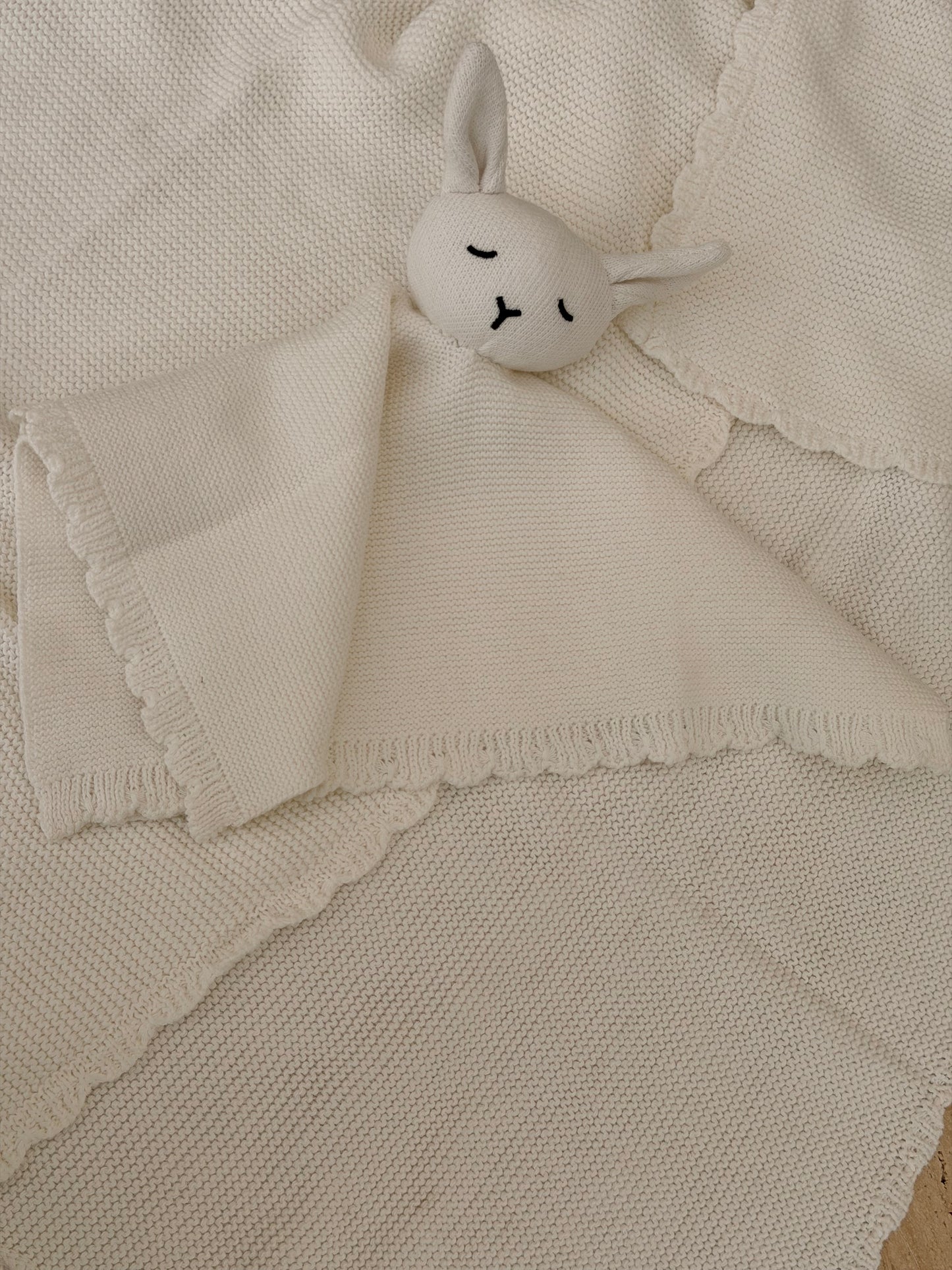 Small white plush bunny toy on a textured beige blanket