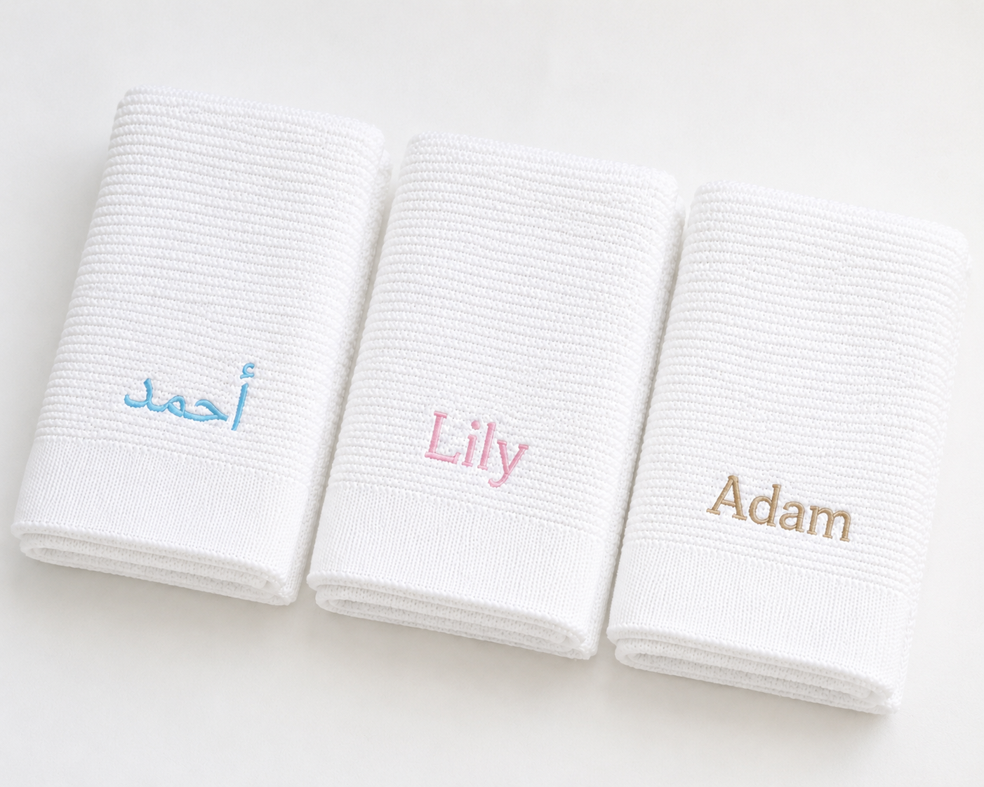 Three white towels with embroidered names 'Ahmed', 'Lily', and 'Adam' on a light background.