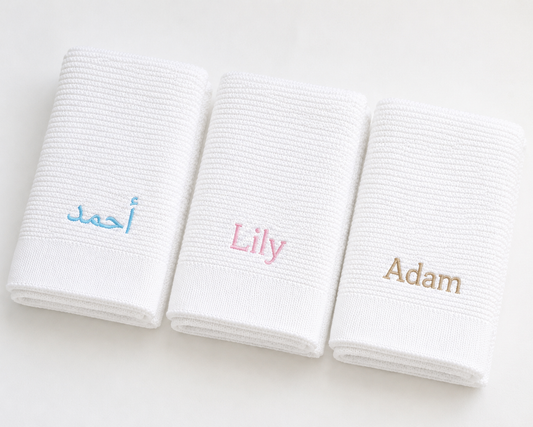 Three white towels with embroidered names 'Ahmed', 'Lily', and 'Adam' on a light background.