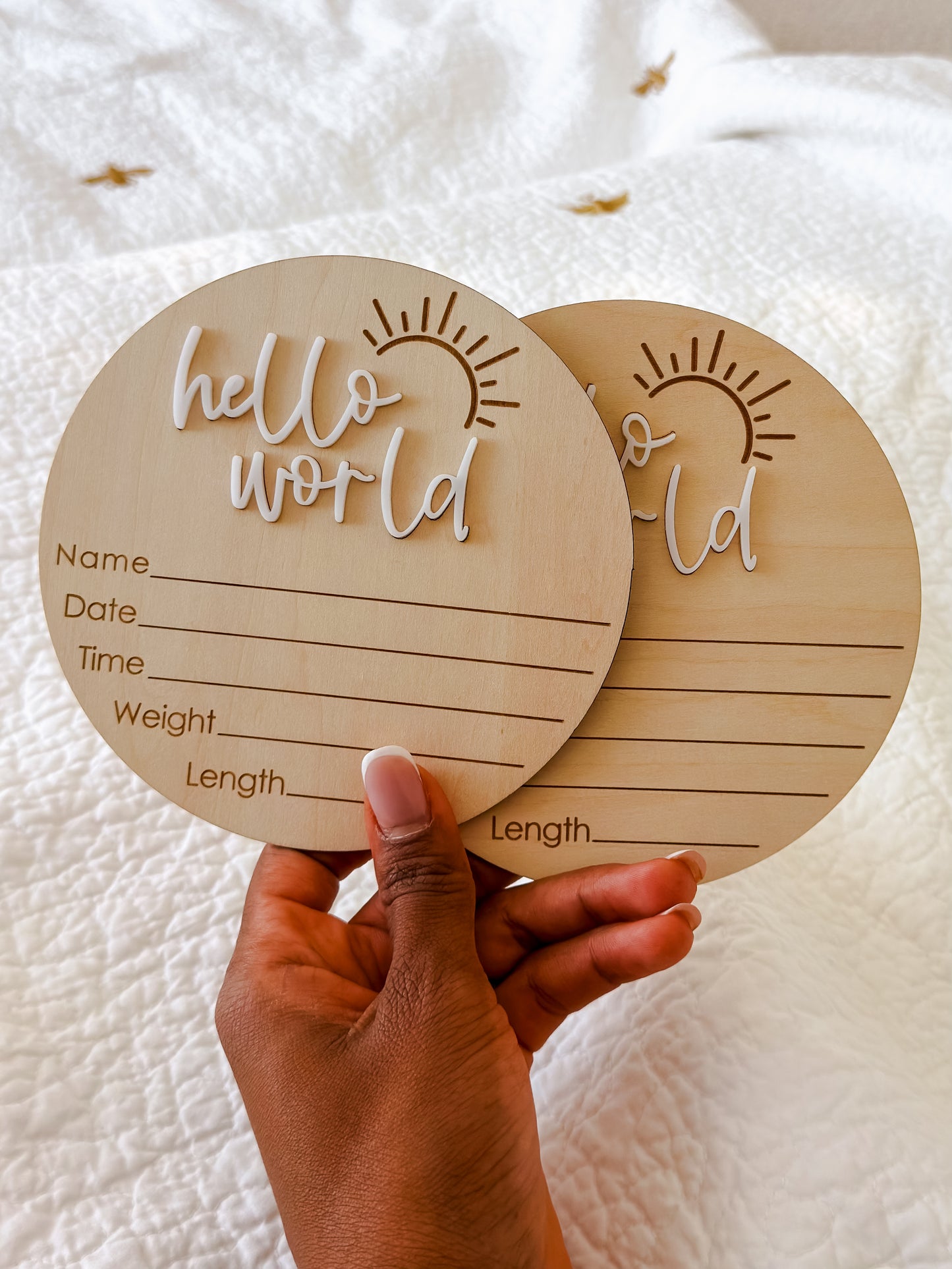 Two wooden circular baby milestone cards with 'hello world' text held by a hand on a white background.