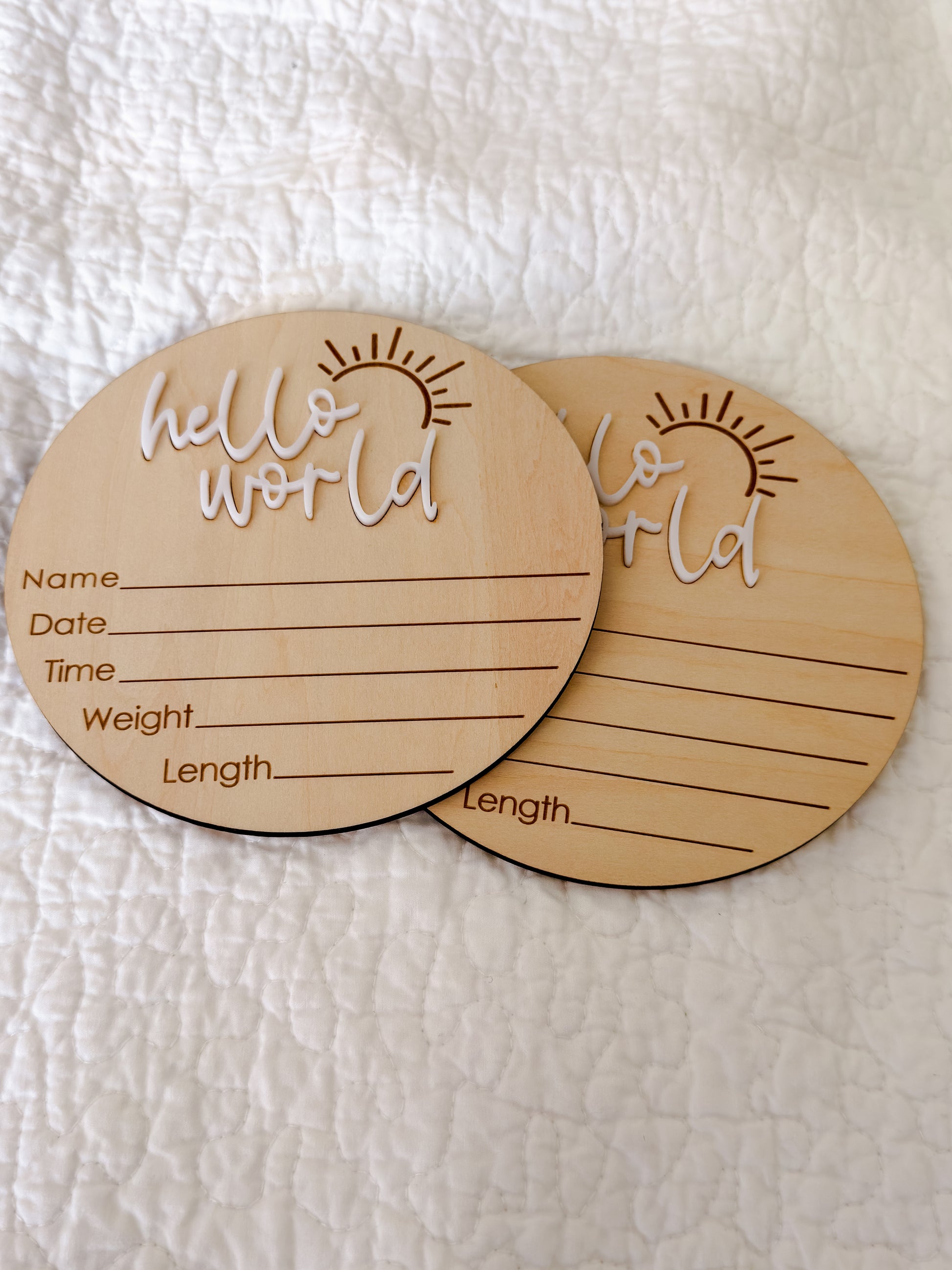 Close-up of beechwood milestone disc with white "hello world" raised lettering and engraved sunburst detail — Maxims Baby Store. UAE
