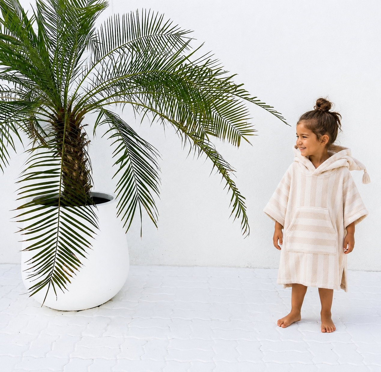 Two children wearing kids hooded beach poncho towels in sandy stripe with tassels playing on the beach
