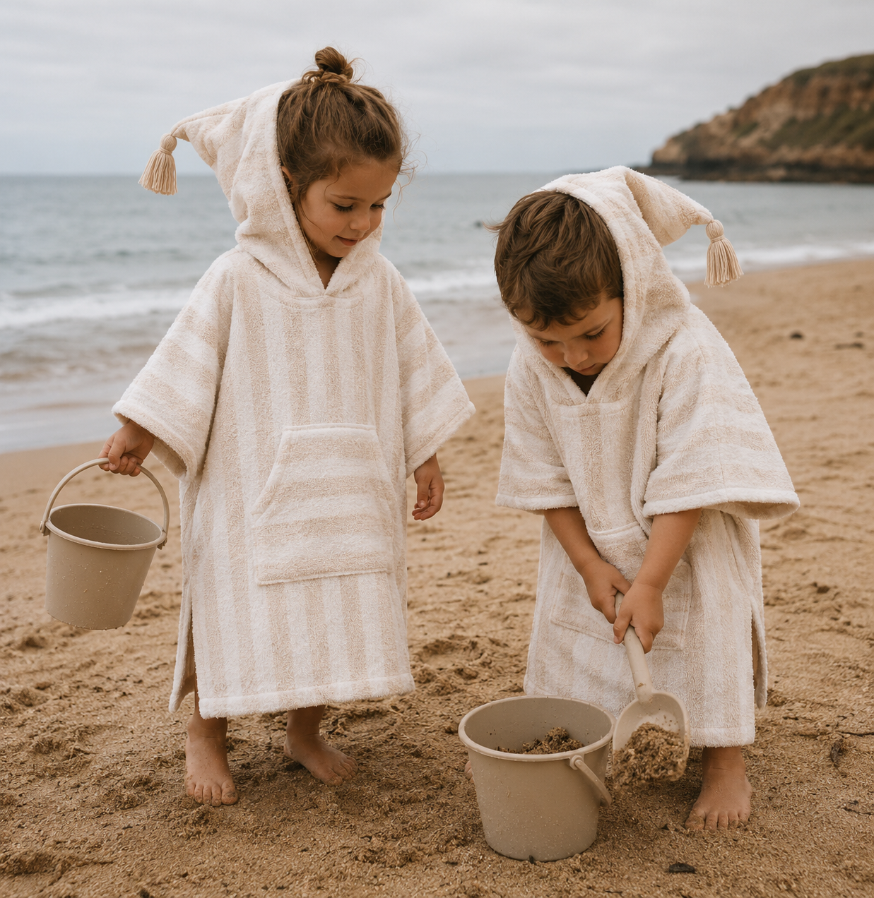 Child wearing kids hooded beach poncho towel sandy stripe with tassel hood standing next to palm tree

