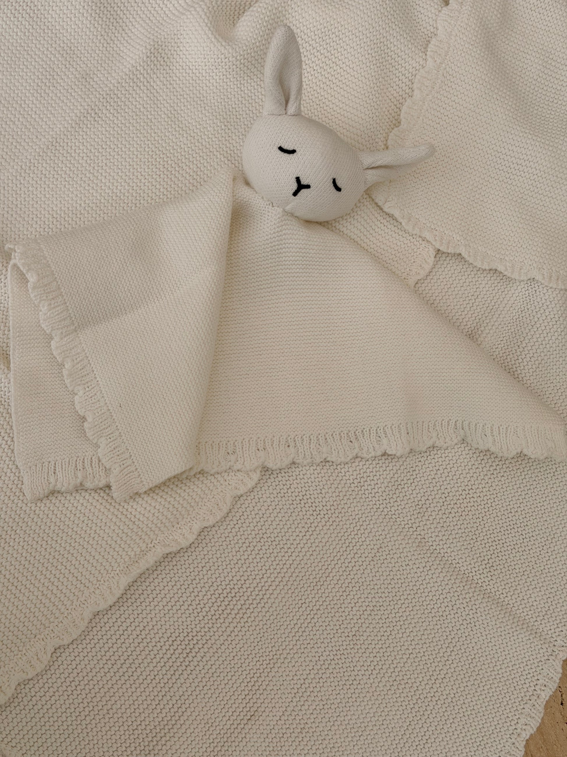 Small white plush bunny toy on a textured beige blanket